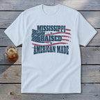 A white short-sleeved t-shirt featuring the text Mississippi Raised American Made and a distressed American flag.
