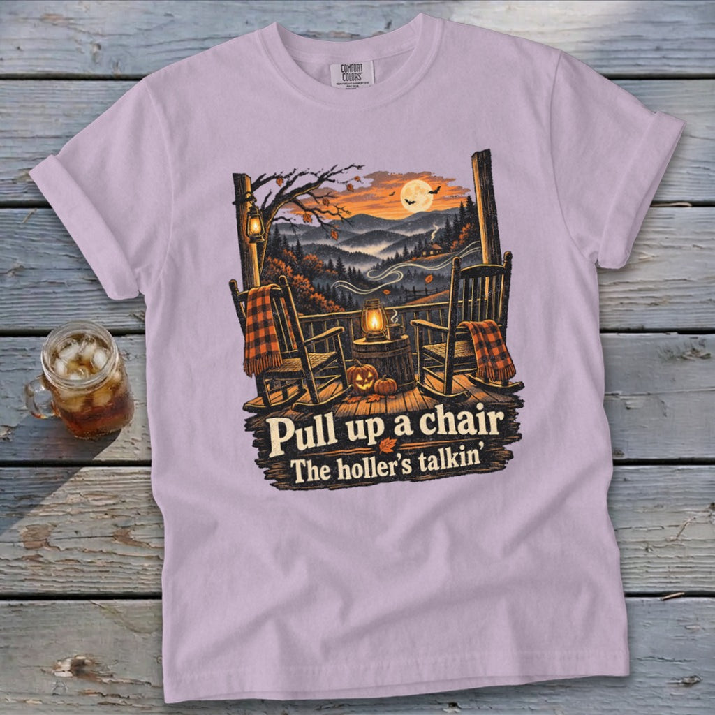 Purple t-shirt with porch scene: rocking chairs, pumpkins, lantern, and text "Pull up a chair. The holler's talkin'."