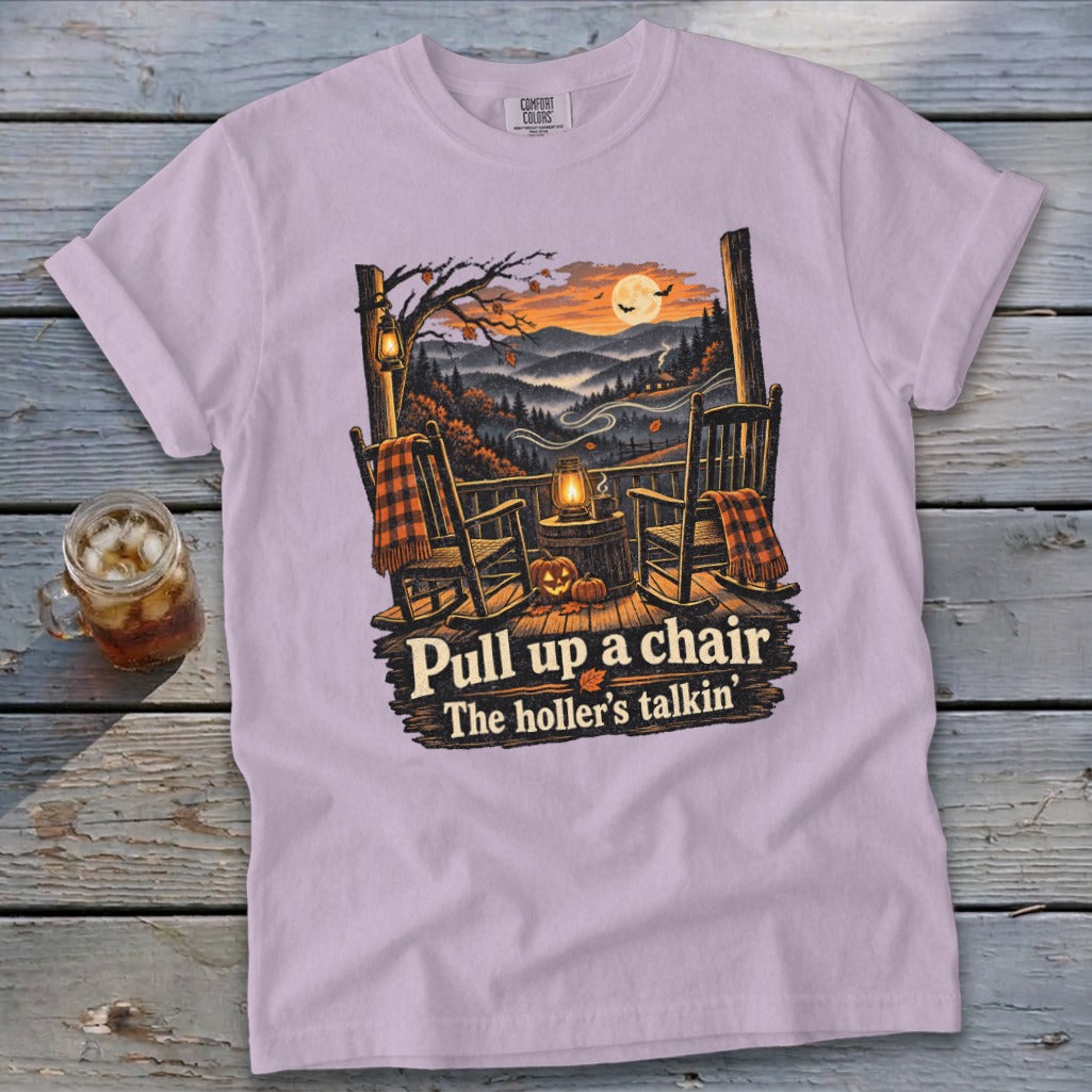 Purple t-shirt with porch scene: rocking chairs, pumpkins, lantern, and text "Pull up a chair. The holler's talkin'."