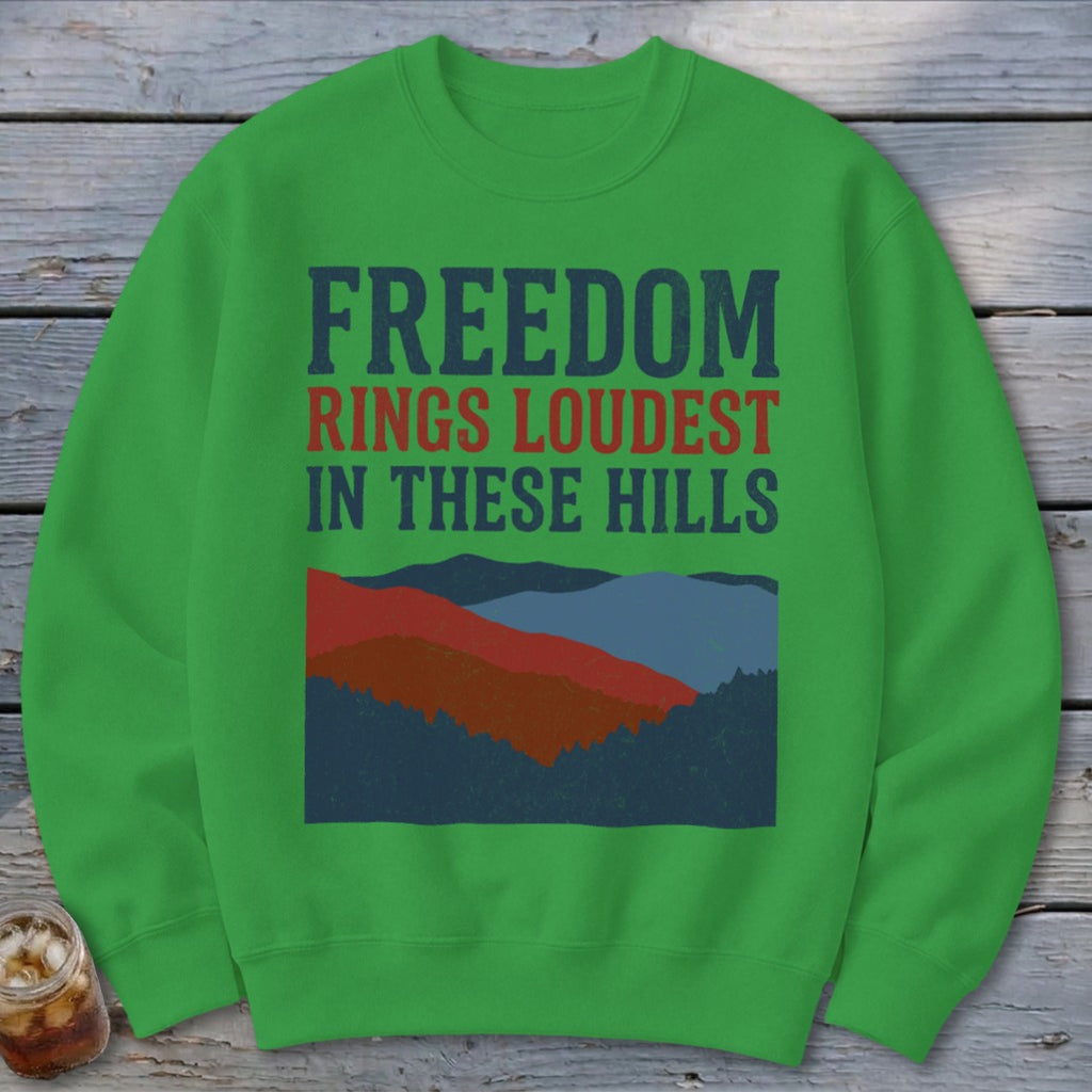A green crewneck sweatshirt featuring the text FREEDOM RINGS LOUDEST IN THESE HILLS above a mountain illustration.
