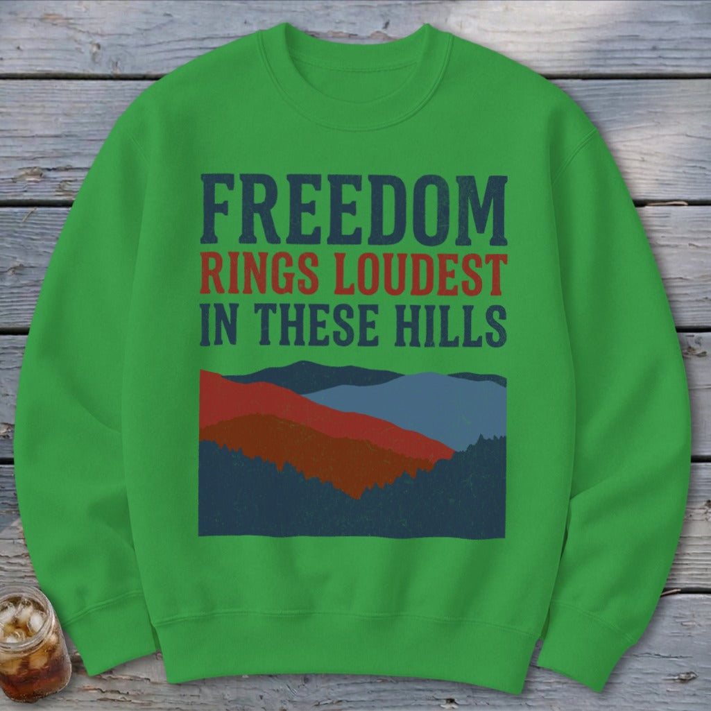 A green crewneck sweatshirt featuring the text FREEDOM RINGS LOUDEST IN THESE HILLS above a mountain illustration.