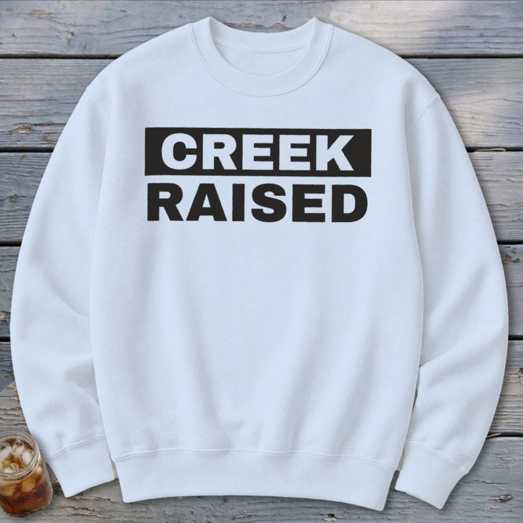 White sweatshirt with black text reading "CREEK RAISED".