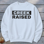 White sweatshirt with black text reading "CREEK RAISED".