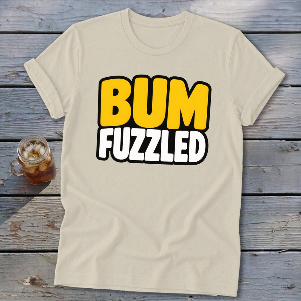 Beige short-sleeve t-shirt with rolled cuffs, featuring the black-outlined text BUM FUZZLED in yellow and white on a wooden background.