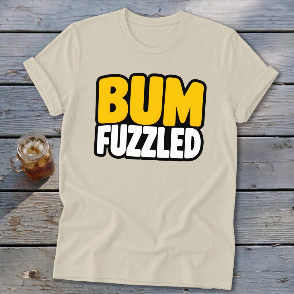 Beige short-sleeve t-shirt with rolled cuffs, featuring the black-outlined text BUM FUZZLED in yellow and white on a wooden background.