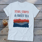 White short-sleeved t-shirt with red, white, and blue text and mountain graphics on a wooden surface.