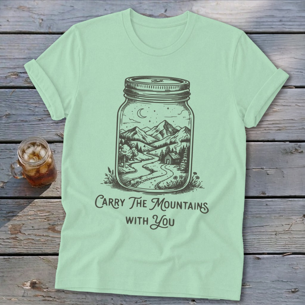 A light green t-shirt featuring a mason jar graphic of a mountain landscape with the text Carry The Mountains With You.