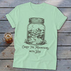 A light green t-shirt featuring a mason jar graphic of a mountain landscape with the text Carry The Mountains With You.