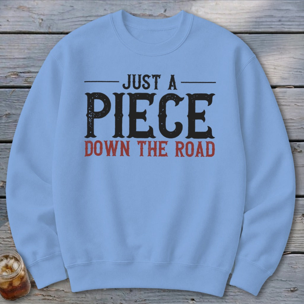 Light blue sweatshirt with distressed text "JUST A PIECE DOWN THE ROAD" in black and red.