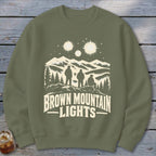 An olive green crewneck sweatshirt featuring a graphic of three figures looking at mountain lights.