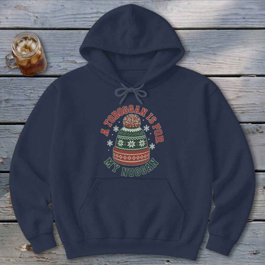 A dark blue hooded sweatshirt featuring a winter hat graphic and the text A TOBOGGAN IS FOR MY NOGGAN.