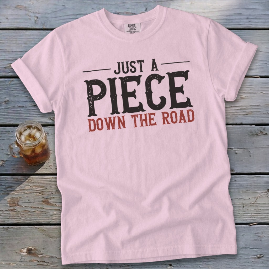 Pink t-shirt with text "JUST A PIECE DOWN THE ROAD"