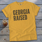 Gold t-shirt with "GEORGIA RAISED" in dark gray lettering