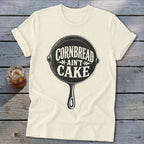 Cream t-shirt with black graphic of a cast iron skillet and text "Cornbread Ain't Cake".