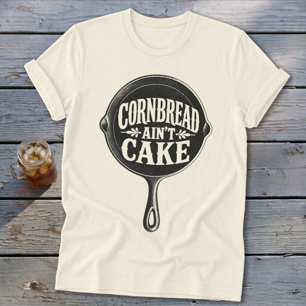 Cream t-shirt with black graphic of a cast iron skillet and text "Cornbread Ain't Cake".