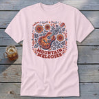 A pink short-sleeve t-shirt features a colorful acoustic guitar graphic with sunflowers and the text "MOUNTAIN MELODIES".