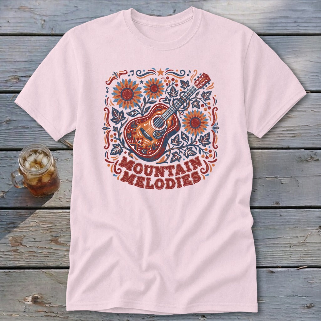 A pink short-sleeve t-shirt features a colorful acoustic guitar graphic with sunflowers and the text "MOUNTAIN MELODIES".