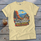 Yellow t-shirt with mountain overlook graphic and text "Peak weekend. Same playlist. New overlook."