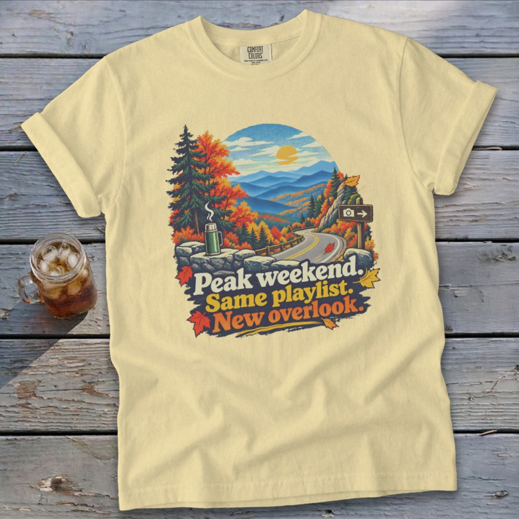 Yellow t-shirt with mountain overlook graphic and text "Peak weekend. Same playlist. New overlook."