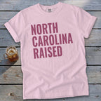 Pink t-shirt with "NORTH CAROLINA RAISED" text in purple.