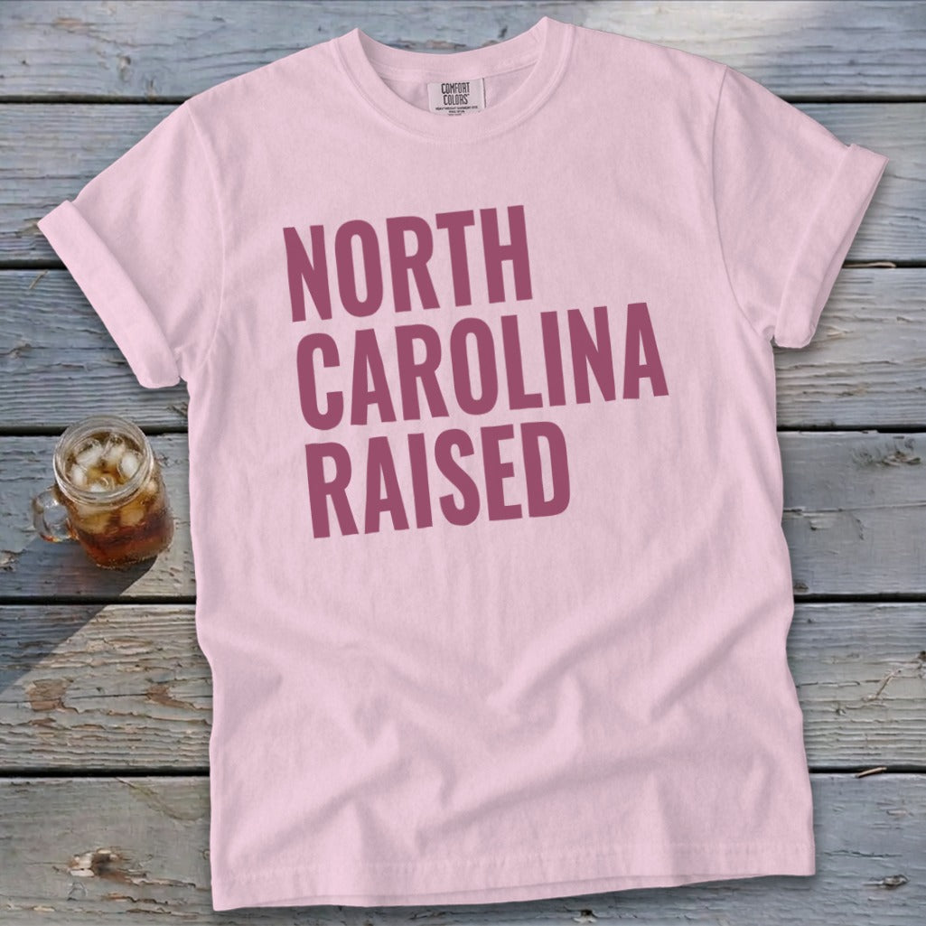 Pink t-shirt with "NORTH CAROLINA RAISED" text in purple.