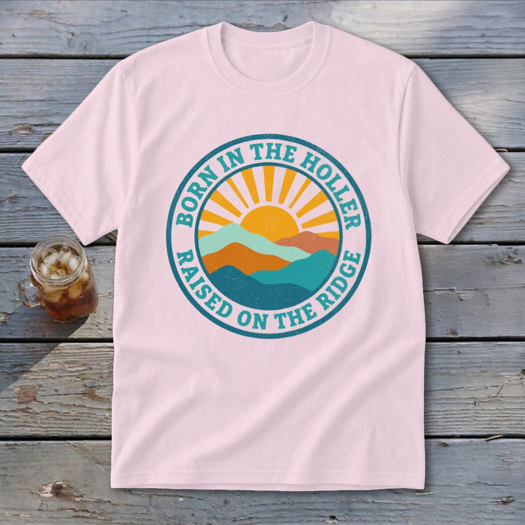Light pink t-shirt with a retro round graphic depicting mountains, a sun, and text saying Born in the Holler Raised on the Ridge.