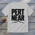 A light gray crewneck t-shirt with bold black text that reads PERT NEAR above a mountain range graphic.