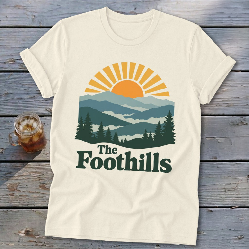 Cream t-shirt with "The Foothills" text and a mountain sunset graphic.