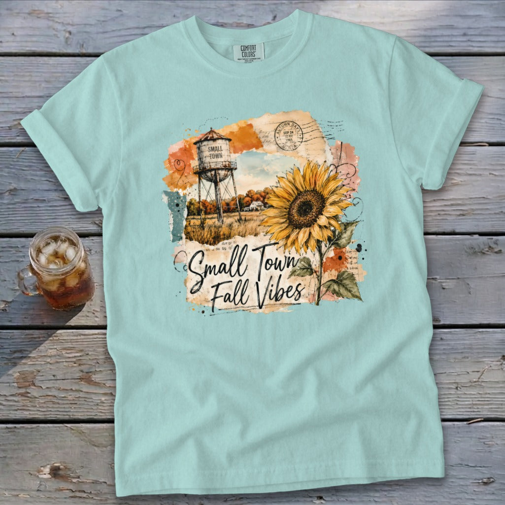 Light blue t-shirt with a graphic of a water tower, sunflower, and the text "Small Town Fall Vibes."