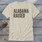 Light beige t-shirt with "ALABAMA RAISED" printed in dark gray text.
