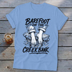 Light blue t-shirt with "BAREFOOT ON THE CREEK BANK" text and illustration.