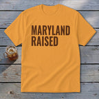 Orange t-shirt with brown text "MARYLAND RAISED" and a glass of iced tea.