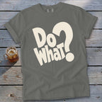 A gray crewneck t-shirt with large white lettering that reads Do What? laid flat on a weathered wooden surface next to a glass of iced tea.