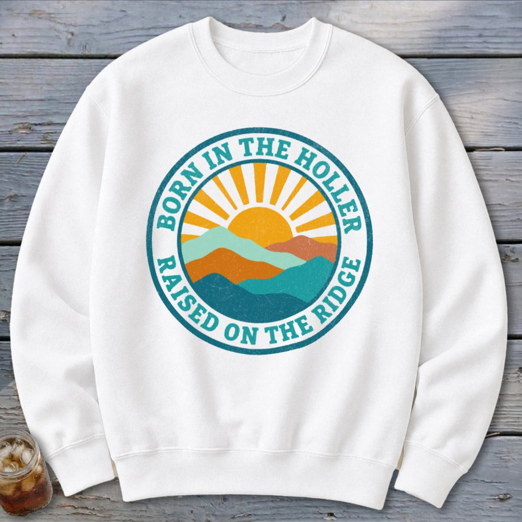 White crewneck sweatshirt with a retro mountain sunrise graphic and the text Born in the Holler, Raised on the Ridge.