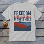 Light gray t-shirt with the red and blue text Freedom Rings Loudest in These Hills above layered mountain graphics.