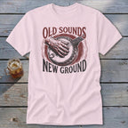 A light pink t-shirt features a vintage graphic of a hand playing a banjo with text reading "OLD SOUNDS NEW GROUND".
