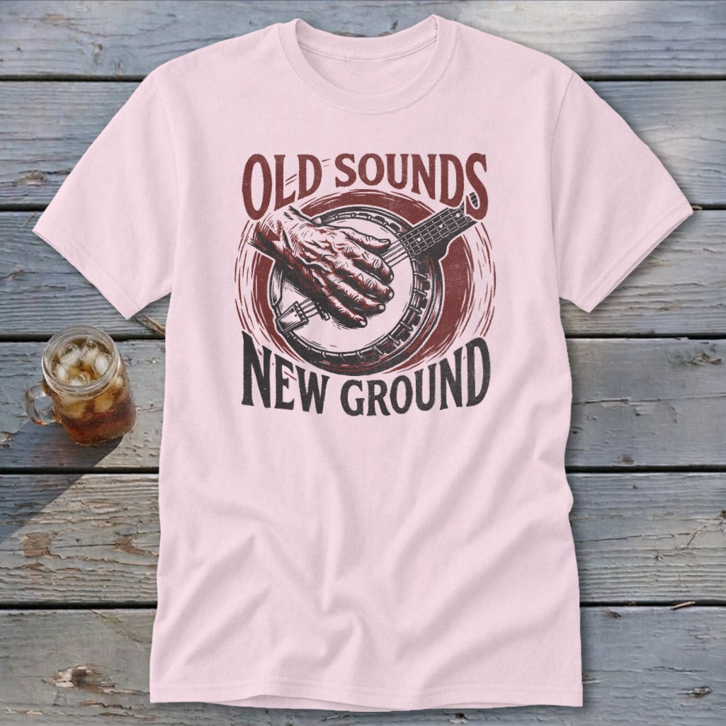 A light pink t-shirt features a vintage graphic of a hand playing a banjo with text reading "OLD SOUNDS NEW GROUND".