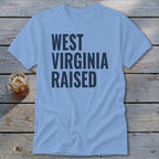 Light blue t-shirt with "WEST VIRGINIA RAISED" in dark blue text.