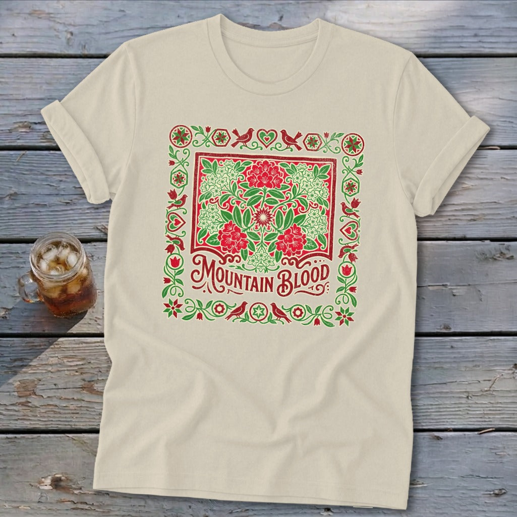 Cream t-shirt with red and green floral border and "Mountain Blood" text.