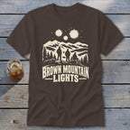 Brown crewneck t-shirt featuring a white graphic of three people looking at glowing lights above mountains.