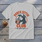 White t-shirt with a bear wearing a cap, drinking from a jar. Text reads "Porch Sittin' Club est. after supper".