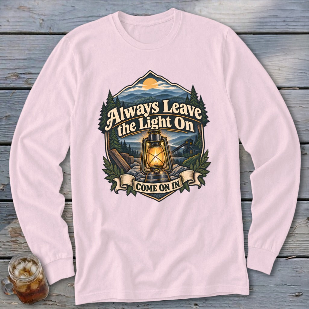 Pink long sleeve shirt with a graphic featuring a lantern and mountains, reading "Always Leave the Light On COME ON IN".