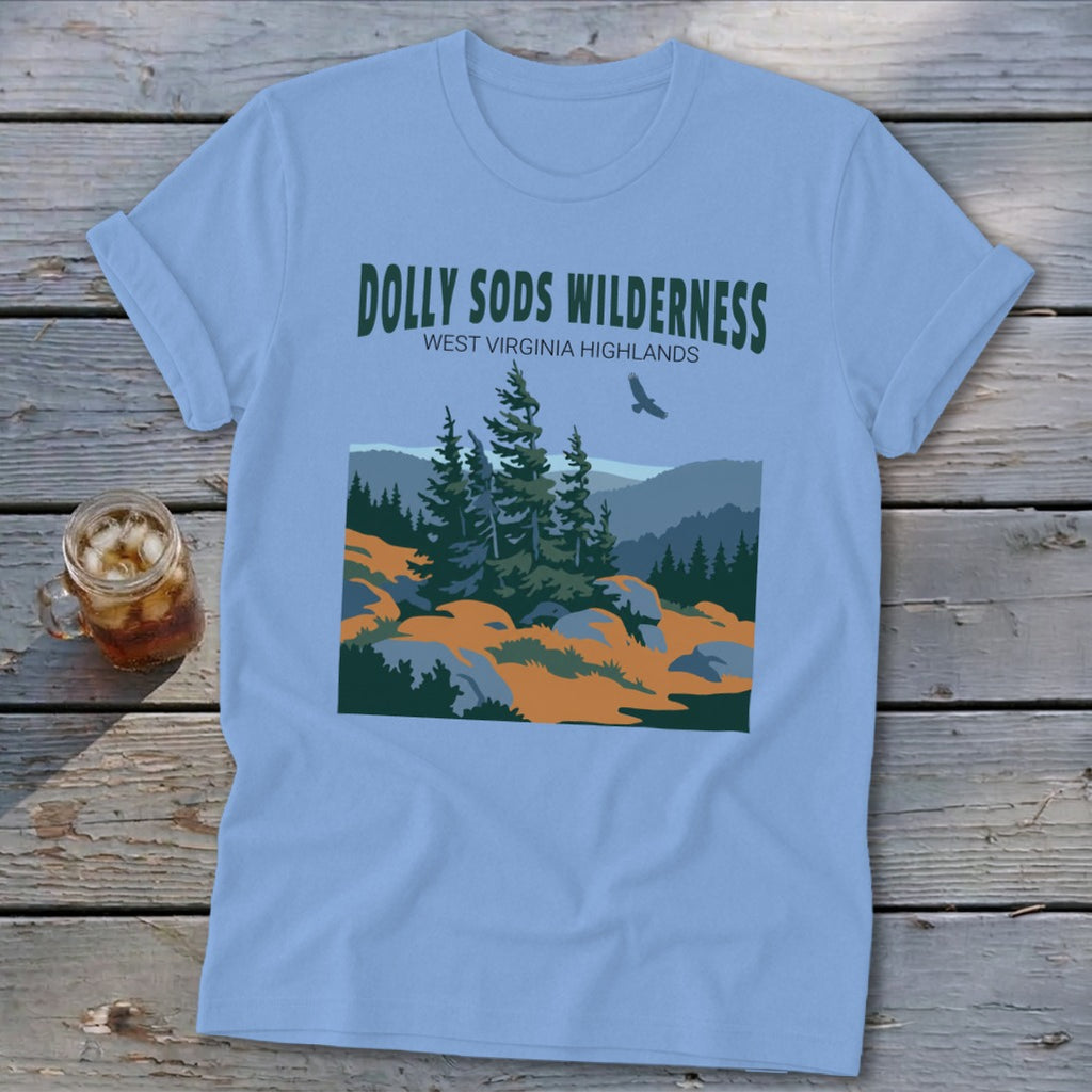 Light blue t-shirt featuring a Dolly Sods Wilderness graphic, laid flat on a wooden surface with a glass of iced tea.