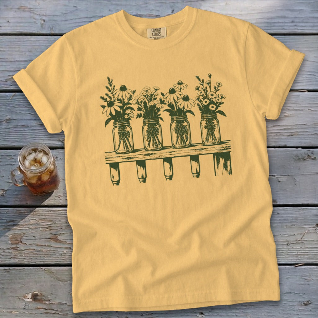 Yellow t-shirt featuring a dark green graphic of four mason jars filled with wildflowers on a wooden shelf.