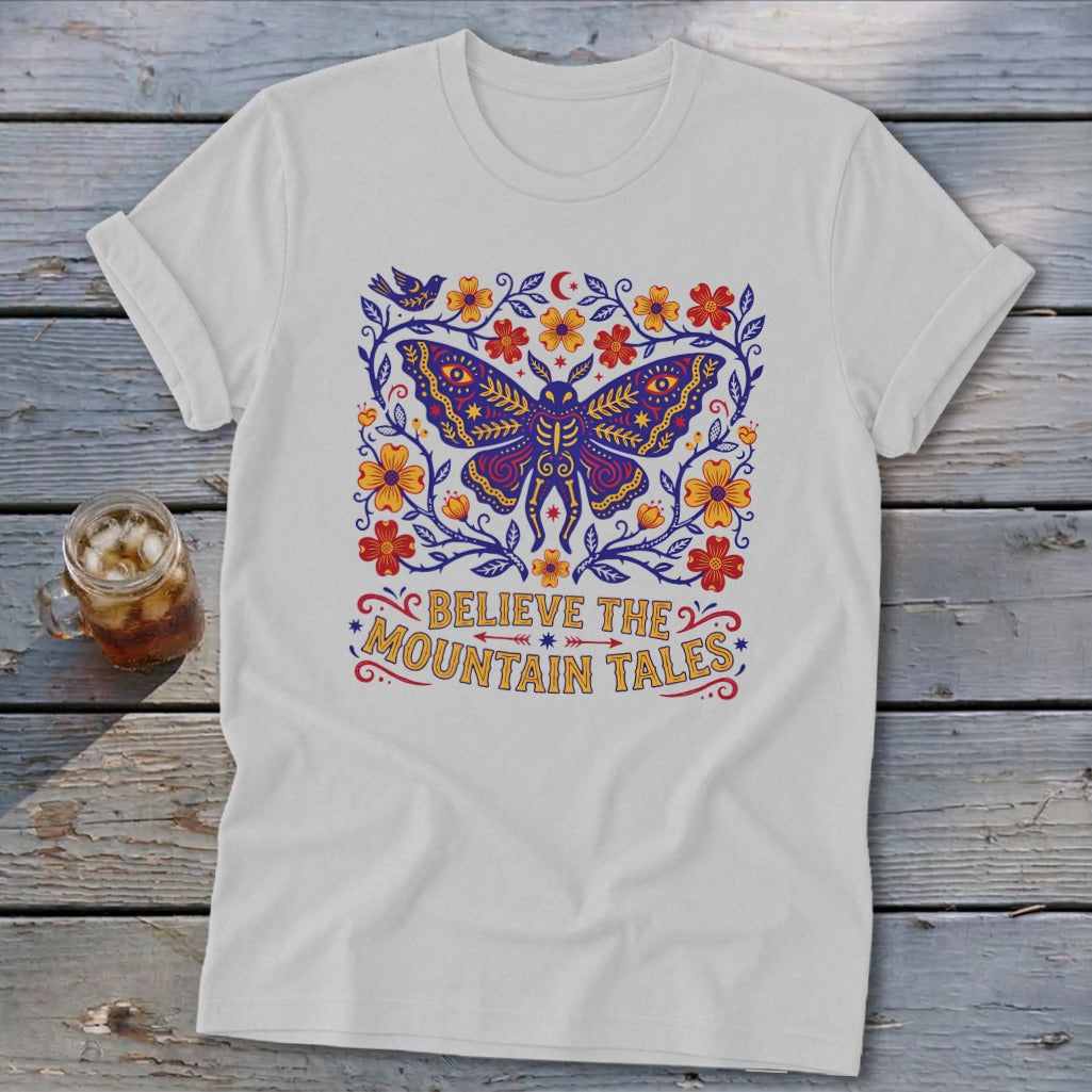 White t-shirt with a purple moth, flowers, bird, and text "BELIEVE THE MOUNTAIN TALES".