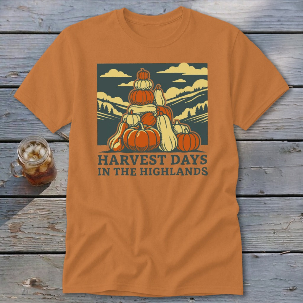 An orange short-sleeve t-shirt with a graphic of stacked pumpkins and the text "HARVEST DAYS IN THE HIGHLANDS."