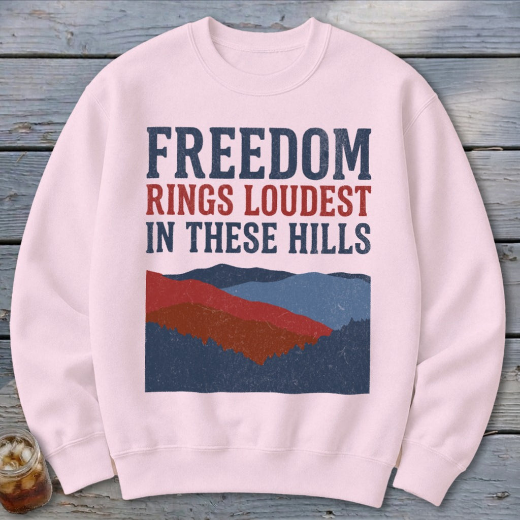 Light pink crewneck sweatshirt featuring distressed patriotic text and a graphic of layered hills.