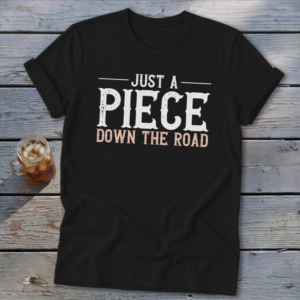Black t-shirt with "JUST A PIECE DOWN THE ROAD" text in white and pink.