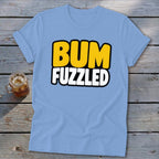 Light blue t-shirt featuring the black-outlined text BUM FUZZLED laid flat on weathered wood.