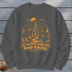 Dark grey sweatshirt with orange mountain landscape graphic and "If you hear whistlin' keep hiking" text.